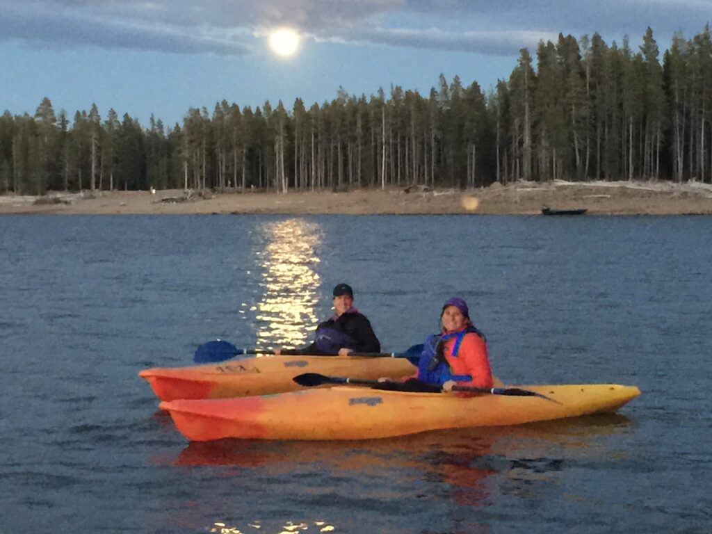 Women in kayaks under a full moon in a calm lake.